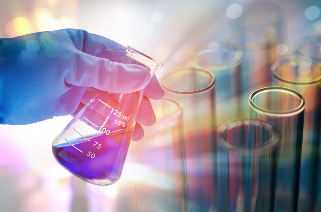 Gloved hand holding a flask of purple liquid in a laboratory
