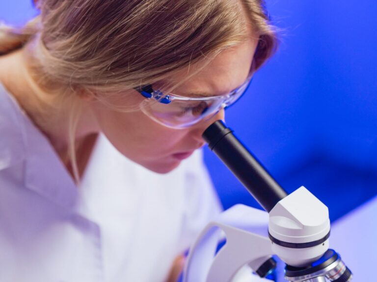 Scientist wearing safety glasses looking into a microscope